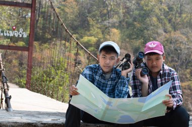 Asian boy held binoculars in hands and doing the bird watching, fish watching and forest observing in local national park, asian children summer vacation concept.