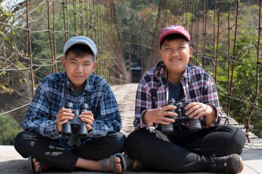 Asian boy held binoculars in hands and doing the bird watching, fish watching and forest observing in local national park, asian children summer vacation concept.