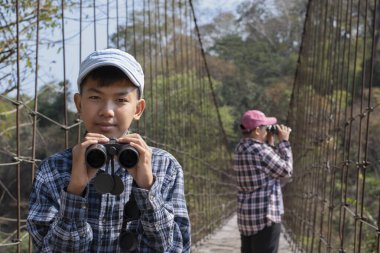 Asian boy held binoculars in hands and doing the bird watching, fish watching and forest observing in local national park, asian children summer vacation concept.
