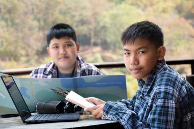 Asian boy held binoculars in hands and doing the bird watching, fish watching and forest observing in local national park, asian children summer vacation concept.