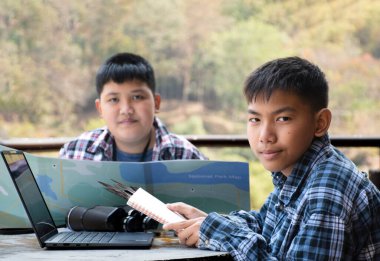 Asian boy held binoculars in hands and doing the bird watching, fish watching and forest observing in local national park, asian children summer vacation concept.