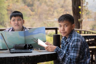 Asian boy held binoculars in hands and doing the bird watching, fish watching and forest observing in local national park, asian children summer vacation concept.