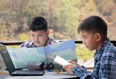 Asian boy held binoculars in hands and doing the bird watching, fish watching and forest observing in local national park, asian children summer vacation concept.
