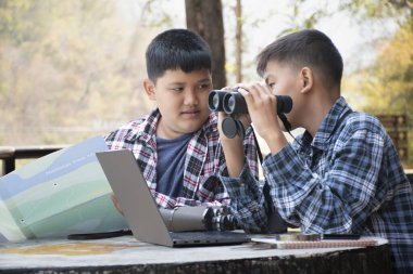 Asian boy held binoculars in hands and doing the bird watching, fish watching and forest observing in local national park, asian children summer vacation concept.