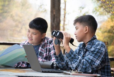 Asian boy held binoculars in hands and doing the bird watching, fish watching and forest observing in local national park, asian children summer vacation concept.