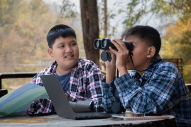 Asian boy held binoculars in hands and doing the bird watching, fish watching and forest observing in local national park, asian children summer vacation concept.