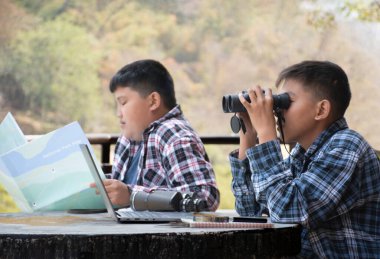 Asian boy held binoculars in hands and doing the bird watching, fish watching and forest observing in local national park, asian children summer vacation concept.