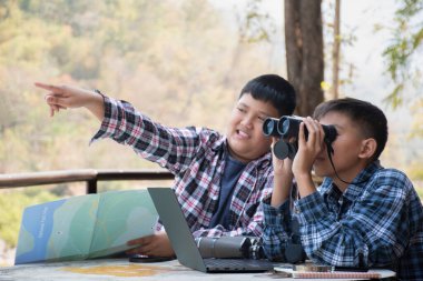 Asian boy held binoculars in hands and doing the bird watching, fish watching and forest observing in local national park, asian children summer vacation concept.