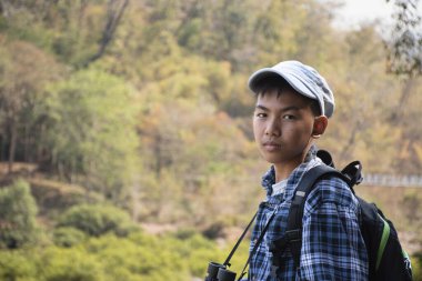 Asian boy held binoculars in hands and doing the bird watching, fish watching and forest observing in local national park, asian children summer vacation concept.