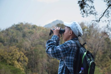 Asian boy held binoculars in hands and doing the bird watching, fish watching and forest observing in local national park, asian children summer vacation concept.