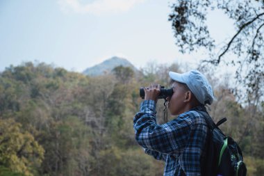 Asian boy held binoculars in hands and doing the bird watching, fish watching and forest observing in local national park, asian children summer vacation concept.