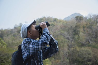Asian boy held binoculars in hands and doing the bird watching, fish watching and forest observing in local national park, asian children summer vacation concept.