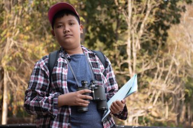 Asian boy held binoculars in hands and doing the bird watching, fish watching and forest observing in local national park, asian children summer vacation concept.
