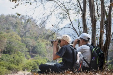 Asian boy held binoculars in hands and doing the bird watching, fish watching and forest observing in local national park, asian children summer vacation concept.