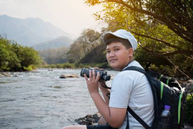 Asian boy held binoculars in hands and doing the bird watching, fish watching and forest observing in local national park, asian children summer vacation concept.