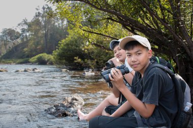 Asian boy held binoculars in hands and doing the bird watching, fish watching and forest observing in local national park, asian children summer vacation concept.