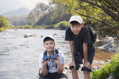 Asian boy held binoculars in hands and doing the bird watching, fish watching and forest observing in local national park, asian children summer vacation concept.