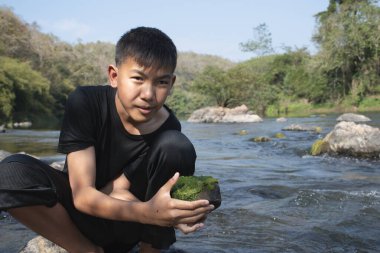 Asian schoolboy holding freshwater algae from diving into the river and pulling it up to study the fertility of the river's nature and including to do freshwater algae in his environment project work.