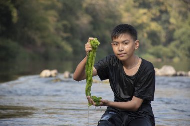 Asian schoolboy holding freshwater algae from diving into the river and pulling it up to study the fertility of the river's nature and including to do freshwater algae in his environment project work.