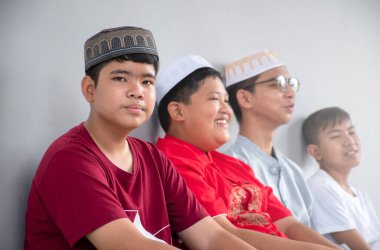 Asian muslim boy sits together with his friends in front of white wall of praying room, selective focus on left boy, concept for lifestyle of muslim boys around the world.