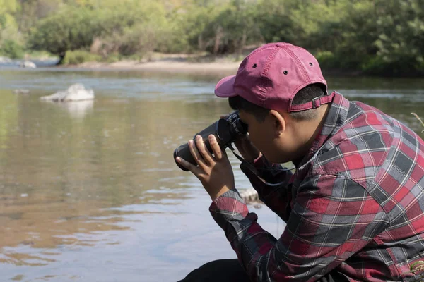 Asian boy held binoculars in hands and doing the bird watching, fish watching and forest observing in local national park, asian children summer vacation concept.