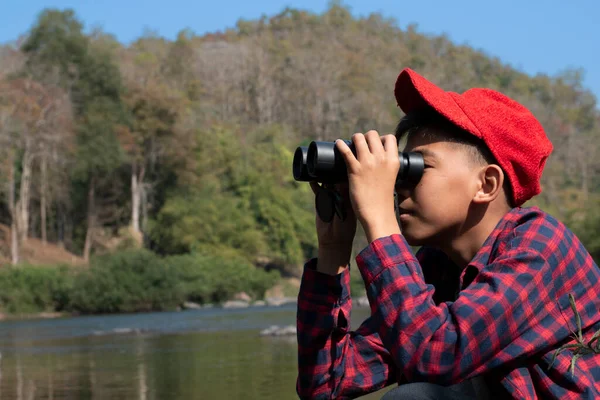 Asian boy held binoculars in hands and doing the bird watching, fish watching and forest observing in local national park, asian children summer vacation concept.