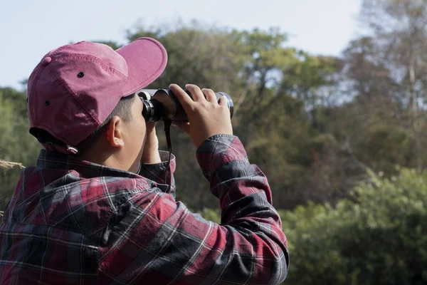Asian boy held binoculars in hands and doing the bird watching, fish watching and forest observing in local national park, asian children summer vacation concept.