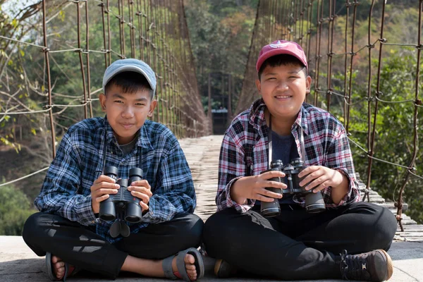 Asian boy held binoculars in hands and doing the bird watching, fish watching and forest observing in local national park, asian children summer vacation concept.