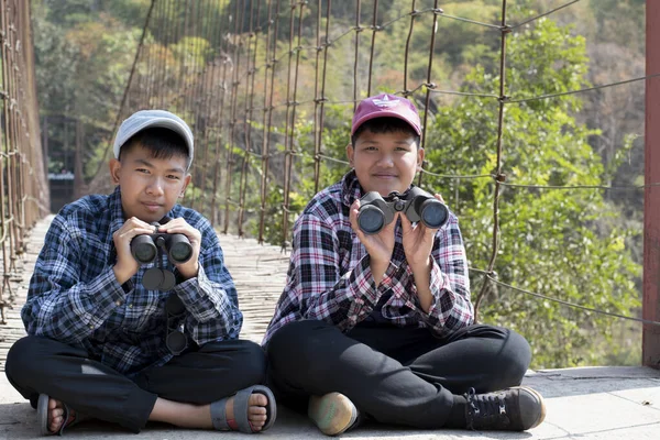 Asian boy held binoculars in hands and doing the bird watching, fish watching and forest observing in local national park, asian children summer vacation concept.
