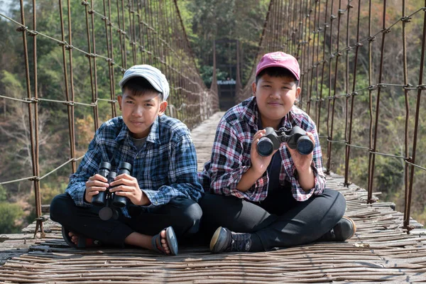 Asian boy held binoculars in hands and doing the bird watching, fish watching and forest observing in local national park, asian children summer vacation concept.