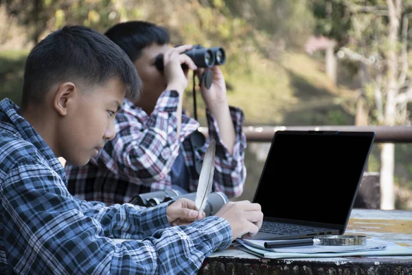 Asian boy held binoculars in hands and doing the bird watching, fish watching and forest observing in local national park, asian children summer vacation concept.