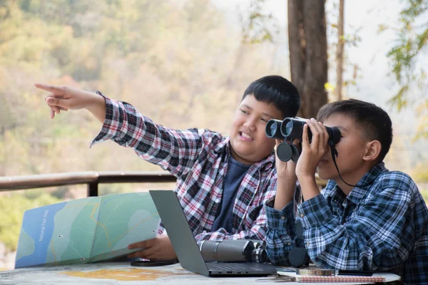 Asian boy held binoculars in hands and doing the bird watching, fish watching and forest observing in local national park, asian children summer vacation concept.
