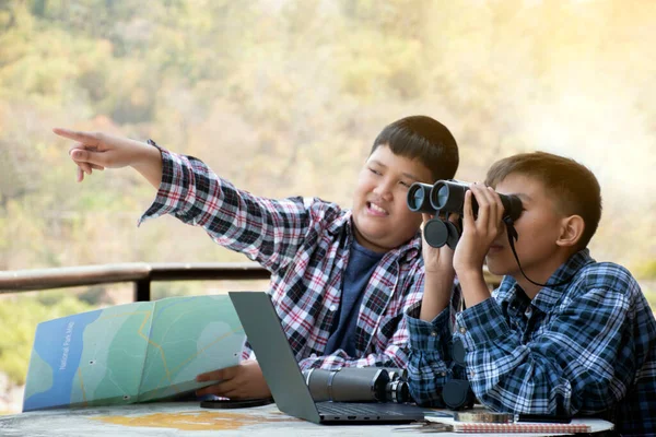 Asian boy held binoculars in hands and doing the bird watching, fish watching and forest observing in local national park, asian children summer vacation concept.