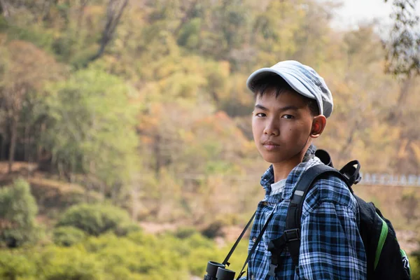 Asian boy held binoculars in hands and doing the bird watching, fish watching and forest observing in local national park, asian children summer vacation concept.