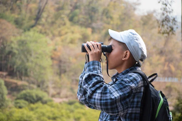 Asian boy held binoculars in hands and doing the bird watching, fish watching and forest observing in local national park, asian children summer vacation concept.