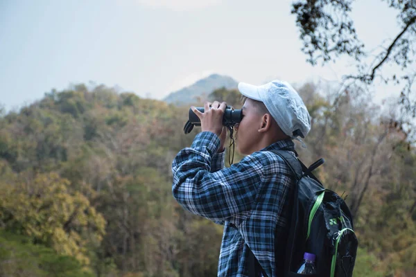 Asian boy held binoculars in hands and doing the bird watching, fish watching and forest observing in local national park, asian children summer vacation concept.