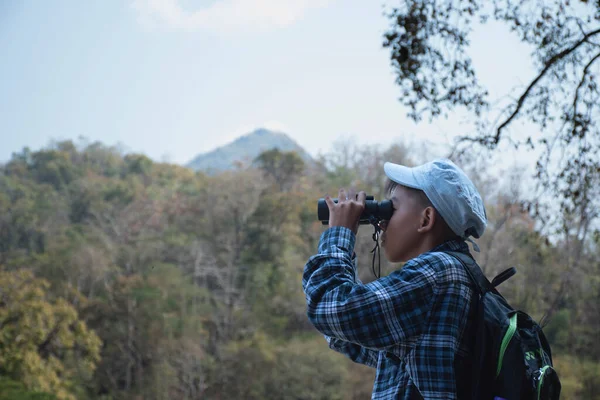 Asian boy held binoculars in hands and doing the bird watching, fish watching and forest observing in local national park, asian children summer vacation concept.