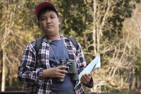Asian boy held binoculars in hands and doing the bird watching, fish watching and forest observing in local national park, asian children summer vacation concept.
