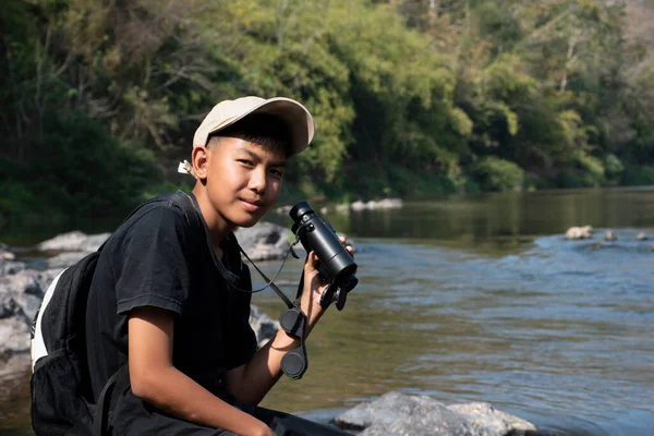 Asian boy held binoculars in hands and doing the bird watching, fish watching and forest observing in local national park, asian children summer vacation concept.