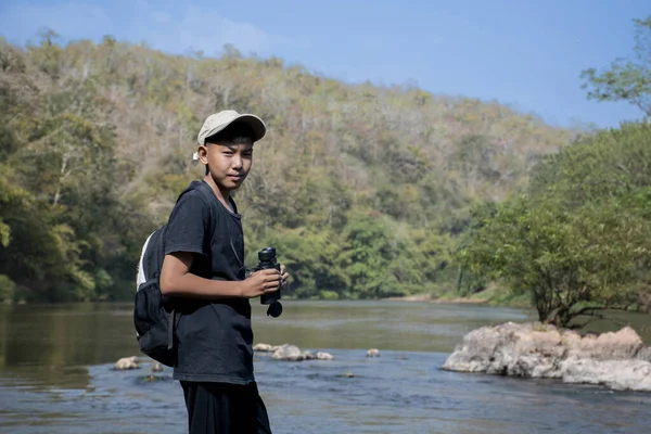 Asian boy held binoculars in hands and doing the bird watching, fish watching and forest observing in local national park, asian children summer vacation concept.