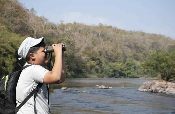 Asian boy held binoculars in hands and doing the bird watching, fish watching and forest observing in local national park, asian children summer vacation concept.
