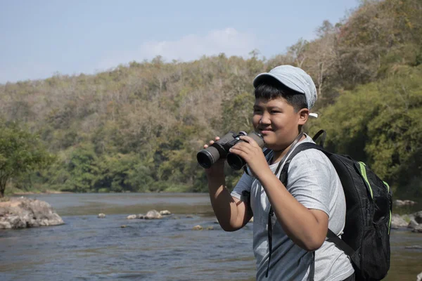 Asian boy held binoculars in hands and doing the bird watching, fish watching and forest observing in local national park, asian children summer vacation concept.