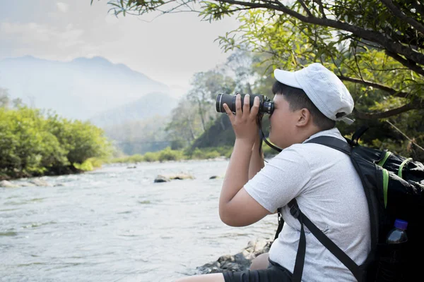 Asian boy held binoculars in hands and doing the bird watching, fish watching and forest observing in local national park, asian children summer vacation concept.