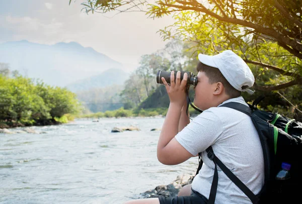 Asian boy held binoculars in hands and doing the bird watching, fish watching and forest observing in local national park, asian children summer vacation concept.