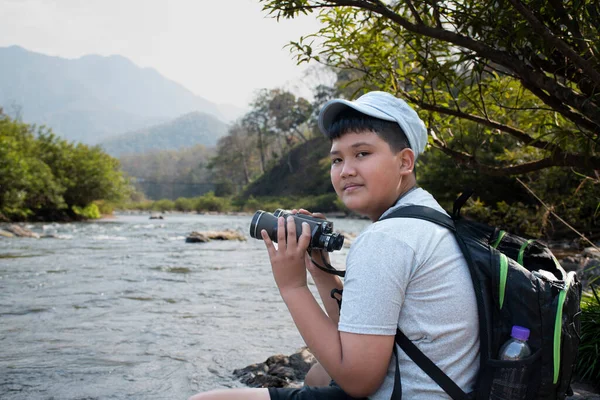 Asian boy held binoculars in hands and doing the bird watching, fish watching and forest observing in local national park, asian children summer vacation concept.