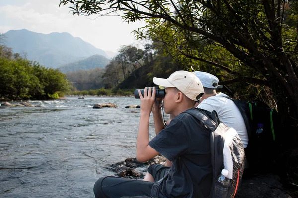 Asian boy held binoculars in hands and doing the bird watching, fish watching and forest observing in local national park, asian children summer vacation concept.
