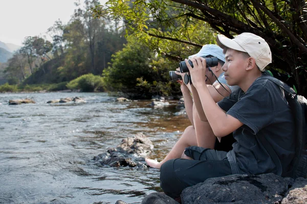 Asian boy held binoculars in hands and doing the bird watching, fish watching and forest observing in local national park, asian children summer vacation concept.
