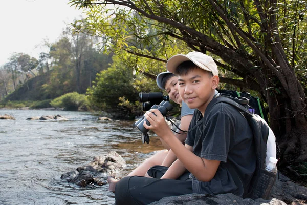 Asian boy held binoculars in hands and doing the bird watching, fish watching and forest observing in local national park, asian children summer vacation concept.