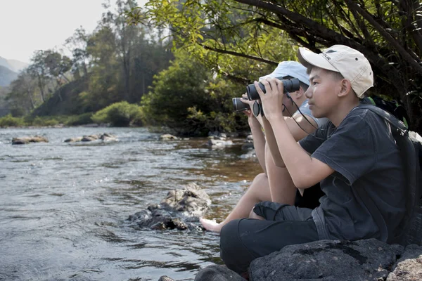 Asian boy held binoculars in hands and doing the bird watching, fish watching and forest observing in local national park, asian children summer vacation concept.