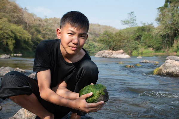 Asian schoolboy holding freshwater algae from diving into the river and pulling it up to study the fertility of the river's nature and including to do freshwater algae in his environment project work.